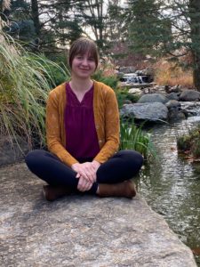 woman sitting cross legged on rock in stream smiling peacefully